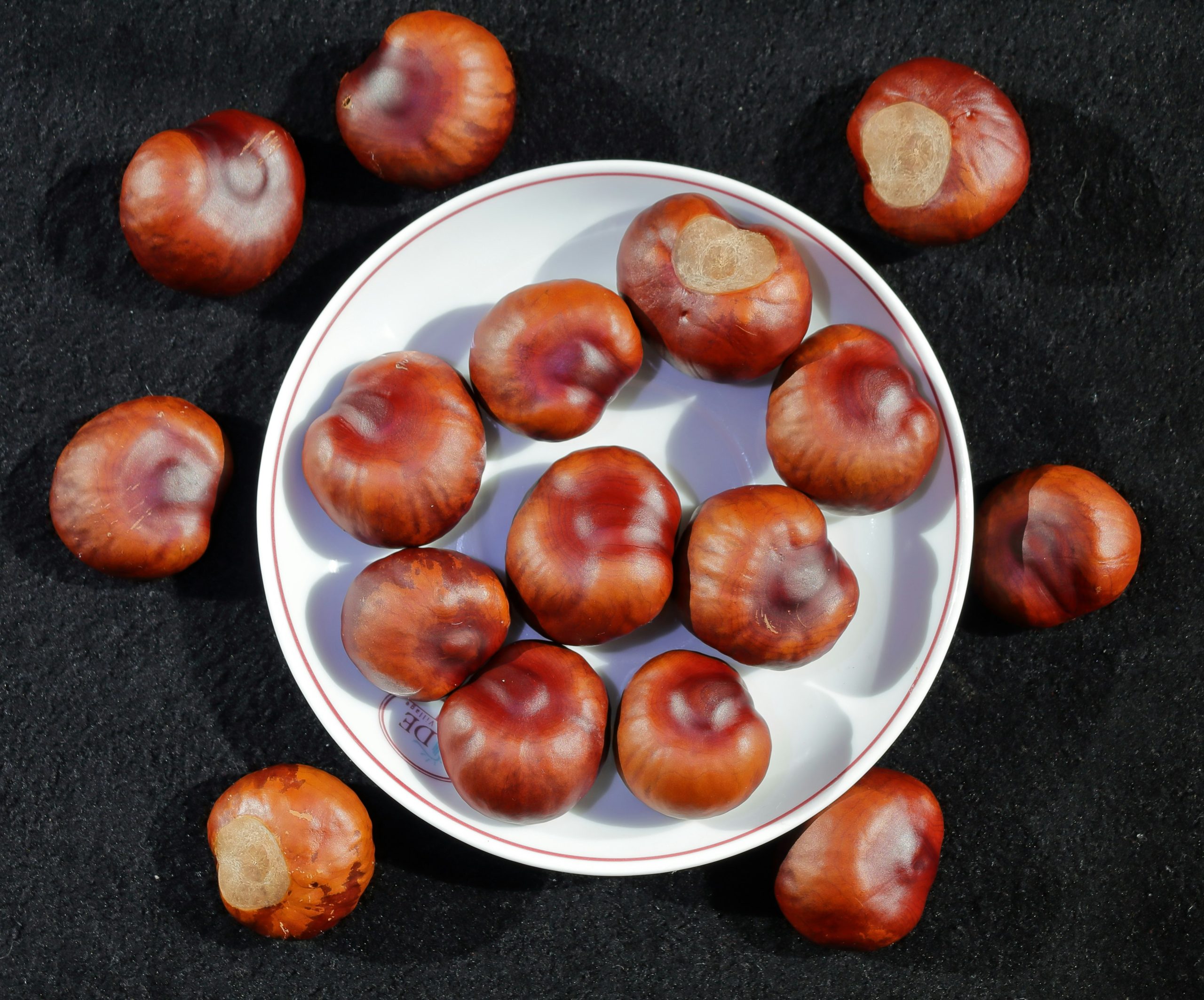 A close-up, high-angle view of a pile of raw, glossy sweet chestnuts with smooth, reddish-brown shells and characteristic pointed tips, showing their natural texture and sheen.